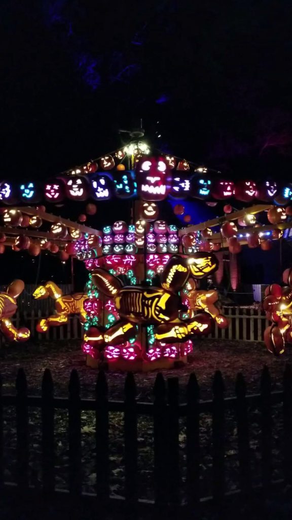 A colorful and illuminated carousel made of carved jack o'lantern pumpkins