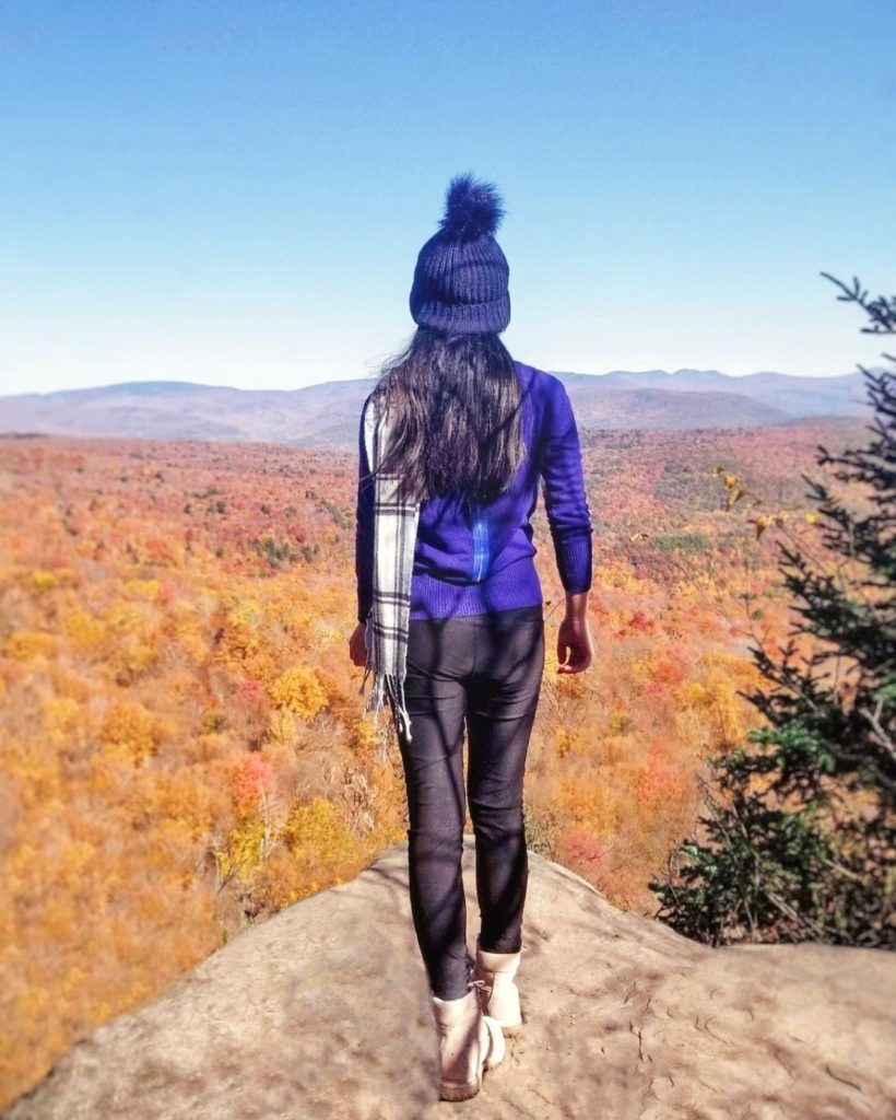 A girl stands on top of a mountain, overlooking fall foliage in the Catskill Mountains.