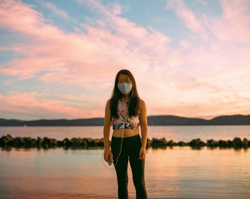 A girl stands along the river at sunset